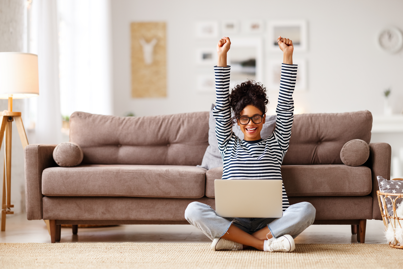 smiling young woman raising her hands, clenching her fists like a winner, in front of her computer at home