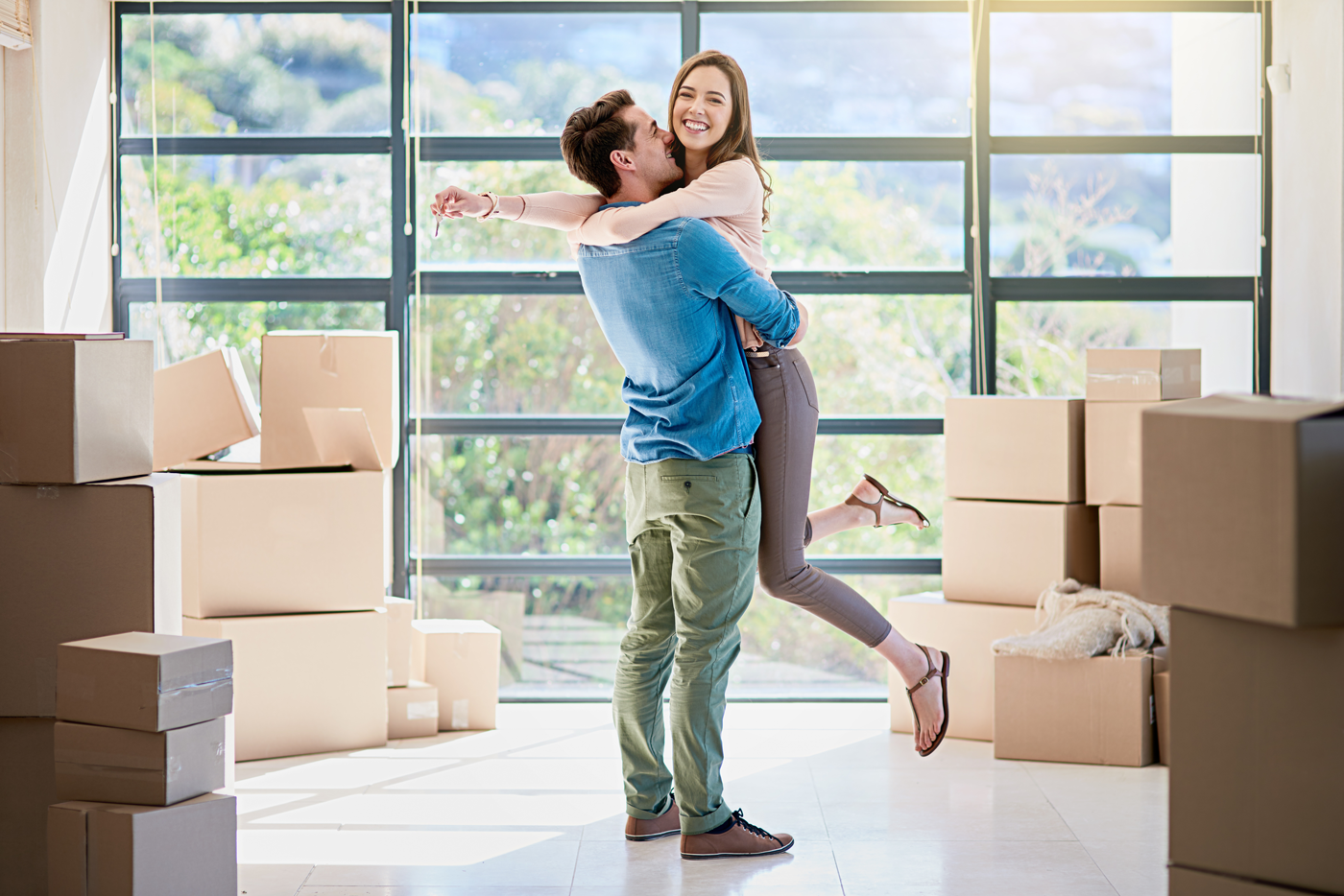 Moving couple: a young man holding his happy wife in his arms, surrounded by moving boxes.
